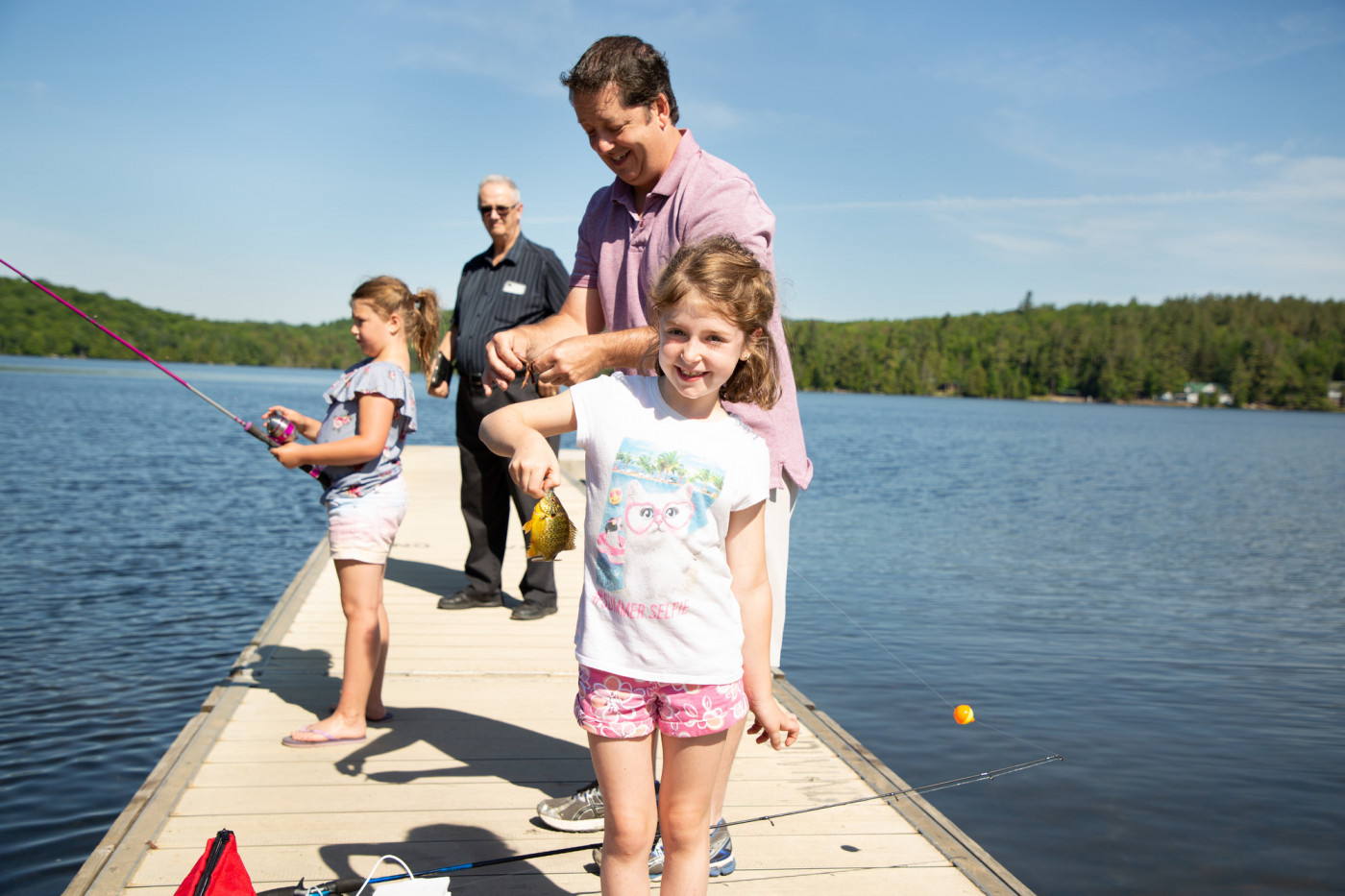 A young girl holds a small fish caught on a dock on a lake.