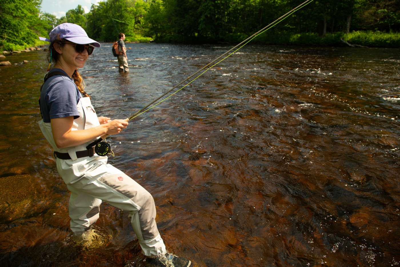 A woman smiles as she casts a fly fishing line